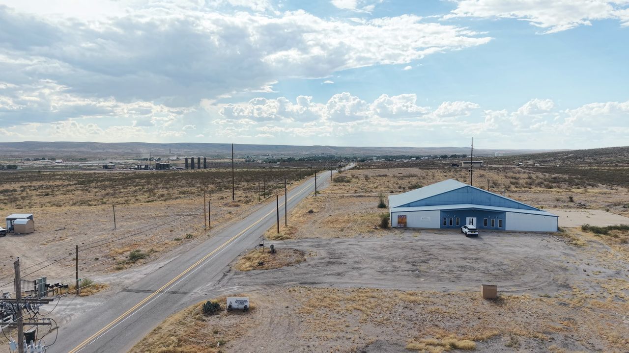 Aerial view of a commercial building and open desert lot beside a highway outside Carlsbad, New Mexico under summer clouds