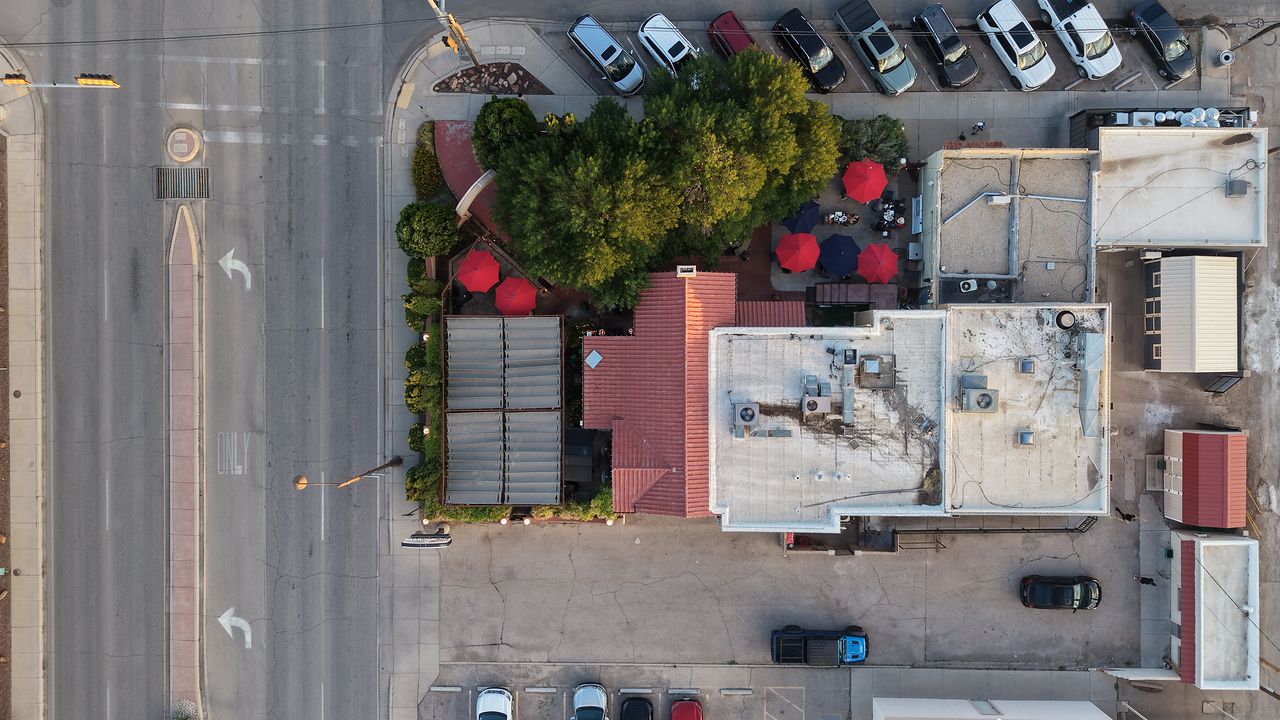 Top-down drone photo of a downtown Carlsbad, NM commercial block showing rooftops, the patio, parking, and Canal Street