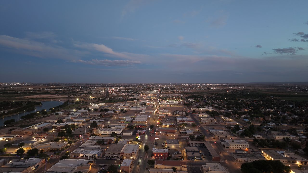 Aerial view of downtown Carlsbad, New Mexico at dusk with the Pecos River on the left and city lights stretching to the horizon