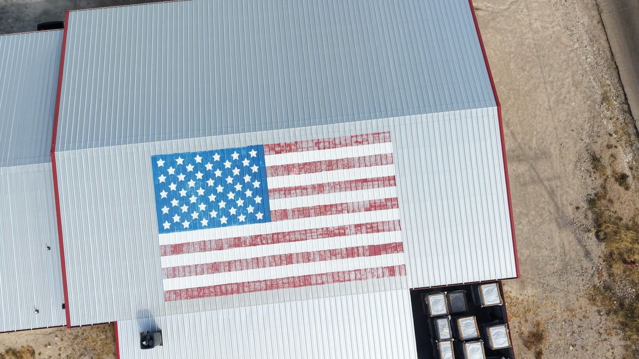 Top-down drone view of a metal commercial building roof with a large painted American flag at Carter's Air Conditioning in Carlsbad, NM