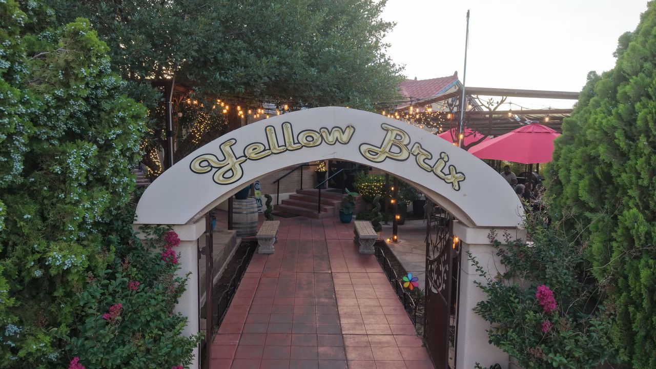 Drone shot at eye level through the Yellow Brix entrance arch and brick walkway toward the patio in Carlsbad, NM